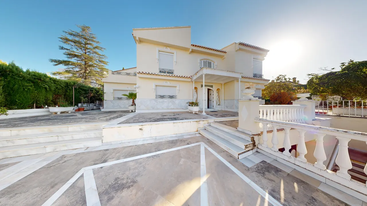Fachada principal de la villa con escalinata y balaustrada blanca en el acceso