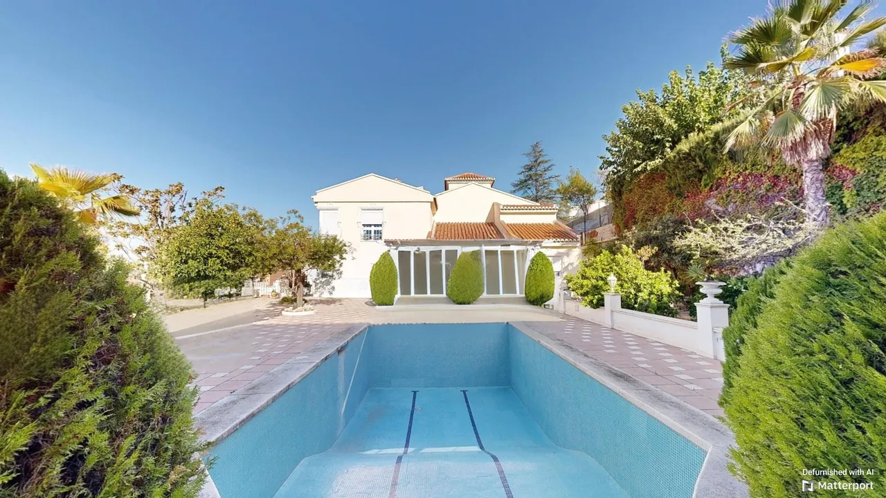Piscina rectangular rodeada de jardín con la vivienda al fondo